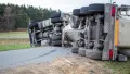 A large semi-truck and its trailer lay overturned on their side across a two-lane road.