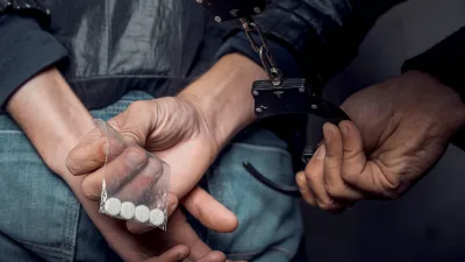 Handcuffed person holding a small bag of white pills