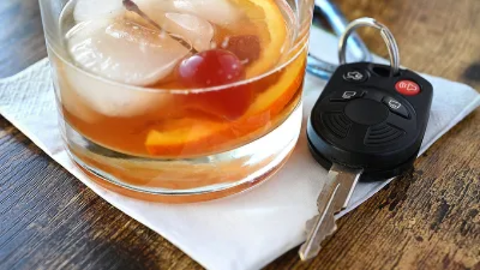 A glass of liquor with car keys in the table.