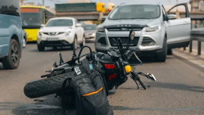 A motorcycle lies on its side in the middle of a busy road following an accident with a car.