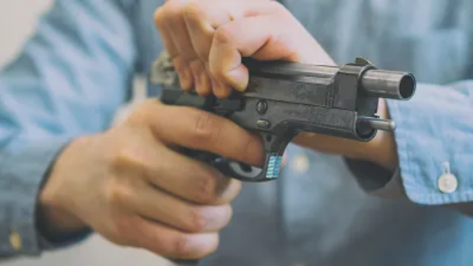 A person's hands racking the slide of a black handgun.