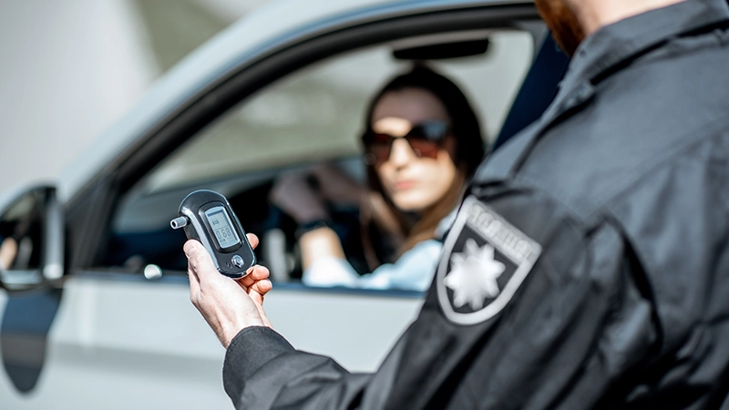 Policeman holding device for checking alcohol intoxication while standing near the stopped car with woman driver.