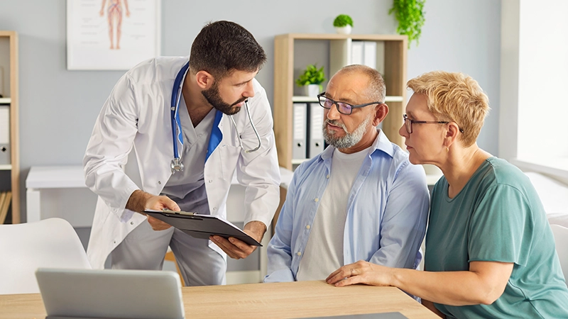 Family doctor explains care plans to elderly patient and companion during medical consultation, discussing diagnosis.